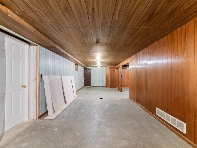 hall featuring unfinished concrete flooring, wood ceiling, visible vents, and wood walls