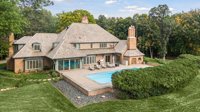 rear view of house with a yard, a fireplace, an outdoor pool, a chimney, and a patio area