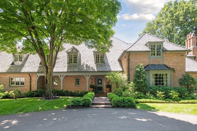 view of front facade with a front yard, a high end roof, and brick siding