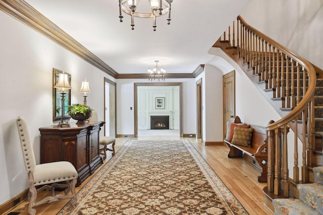 foyer entrance with light wood-type flooring, a notable chandelier, ornamental molding, baseboards, and stairs