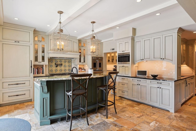 kitchen with stone tile floors, a kitchen island with sink, stainless steel appliances, decorative light fixtures, and tasteful backsplash