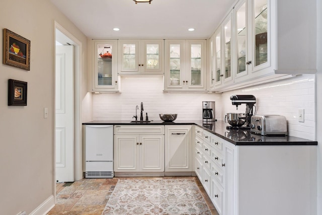 kitchen with backsplash, dark countertops, stone tile floors, white cabinetry, and white dishwasher