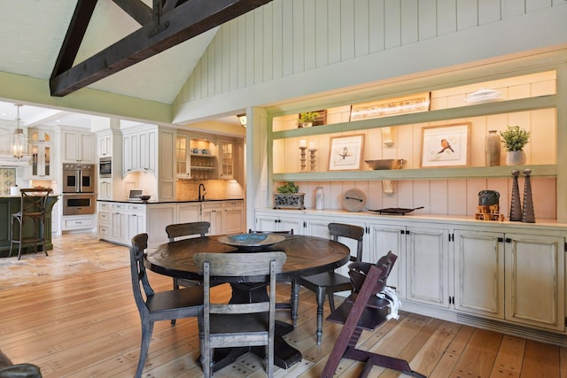 dining room with beam ceiling, high vaulted ceiling, light wood-style floors, and a chandelier