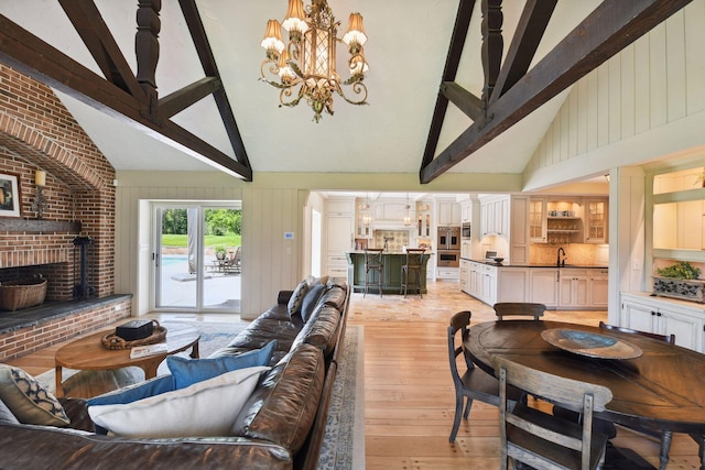 living area featuring an inviting chandelier, beam ceiling, a fireplace, and light wood finished floors