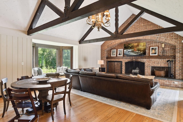 living room with light wood-type flooring, beam ceiling, a fireplace, an inviting chandelier, and high vaulted ceiling