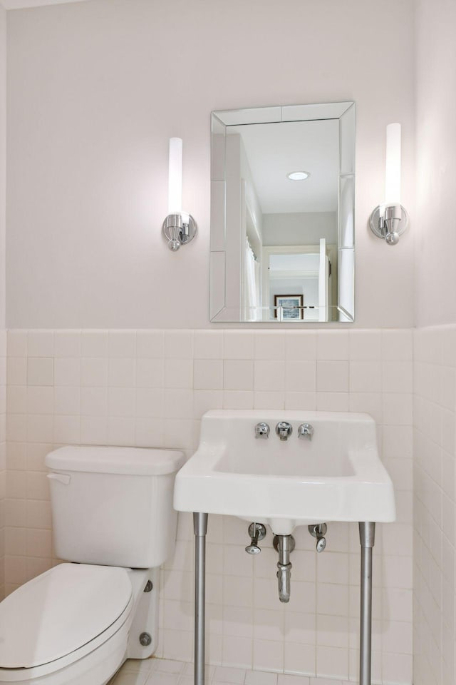 bathroom with a wainscoted wall, toilet, and tile walls