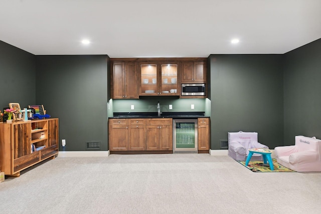 bar featuring stainless steel microwave, beverage cooler, light colored carpet, indoor wet bar, and a sink