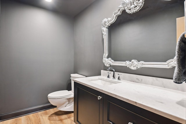 half bathroom with toilet, vanity, and wood finished floors