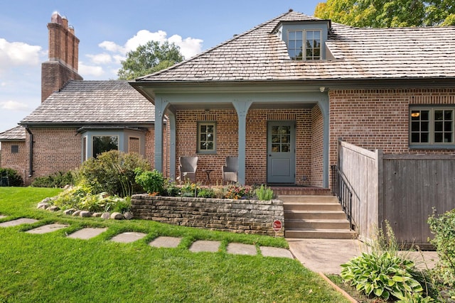 exterior space featuring brick siding, fence, a front yard, covered porch, and a chimney