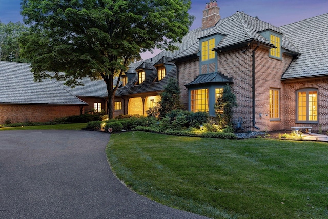 view of front facade with a front yard, brick siding, driveway, and a chimney