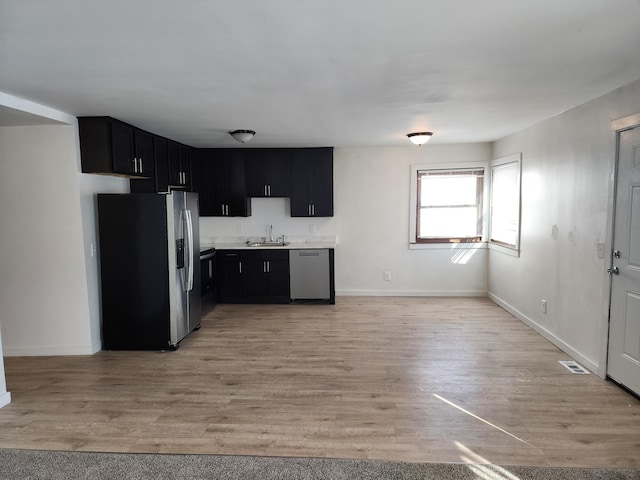 kitchen featuring a sink, appliances with stainless steel finishes, light wood-style floors, and dark cabinets