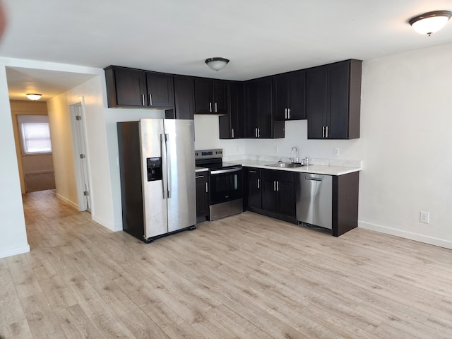 kitchen featuring light wood-type flooring, a sink, stainless steel appliances, light countertops, and baseboards