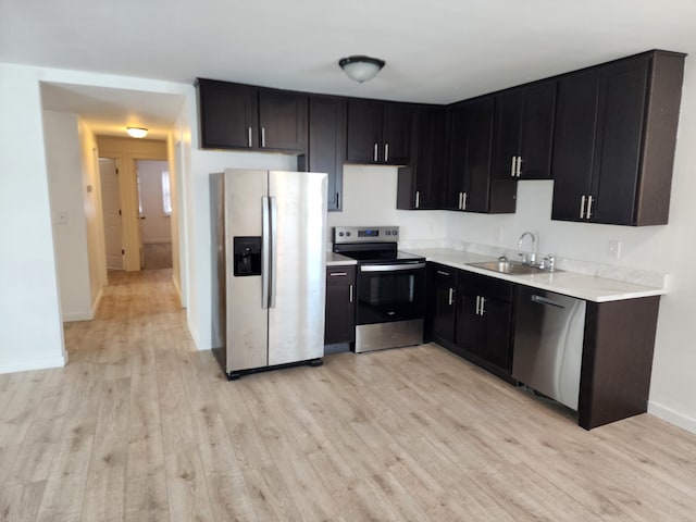 kitchen featuring light countertops, light wood-style flooring, dark cabinetry, stainless steel appliances, and a sink