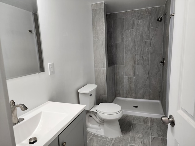 bathroom featuring toilet, tiled shower, and vanity