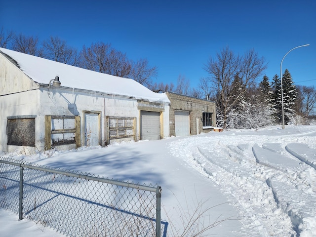 view of snow covered exterior featuring an outdoor structure, an attached garage, and fence