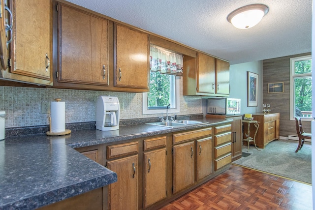 kitchen featuring brown cabinetry, dark countertops, a healthy amount of sunlight, and a sink