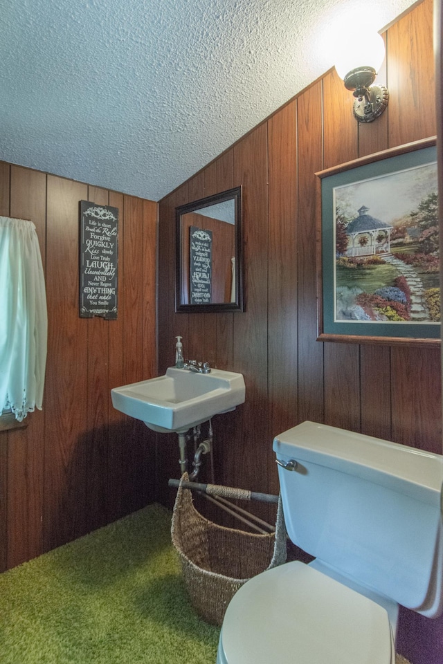 half bath with toilet, a sink, wooden walls, vaulted ceiling, and a textured ceiling