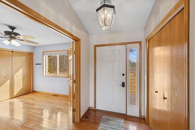 entrance foyer with visible vents, ceiling fan with notable chandelier, a textured ceiling, light wood finished floors, and baseboards