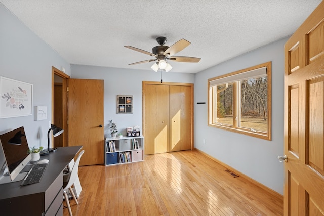 office area with light wood-type flooring, visible vents, a textured ceiling, and a ceiling fan