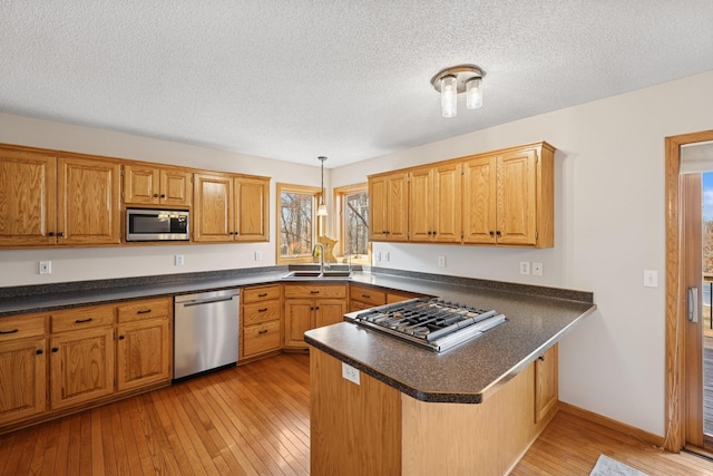 kitchen featuring dark countertops, light wood-style flooring, a peninsula, stainless steel appliances, and a sink