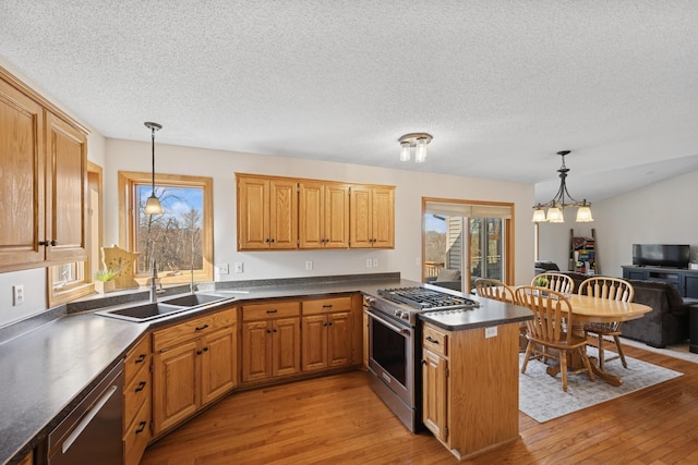 kitchen with dark countertops, light wood finished floors, appliances with stainless steel finishes, a peninsula, and a sink