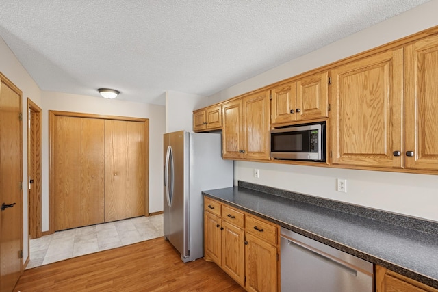 kitchen featuring dark countertops, appliances with stainless steel finishes, light wood-style flooring, and a textured ceiling