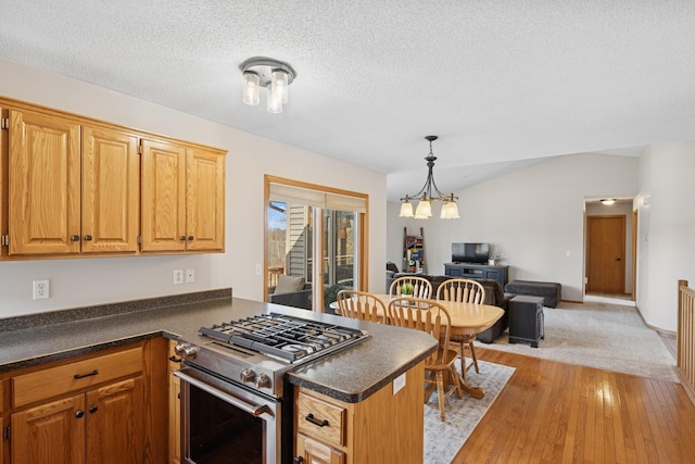 kitchen with dark countertops, light wood finished floors, vaulted ceiling, a peninsula, and gas stove