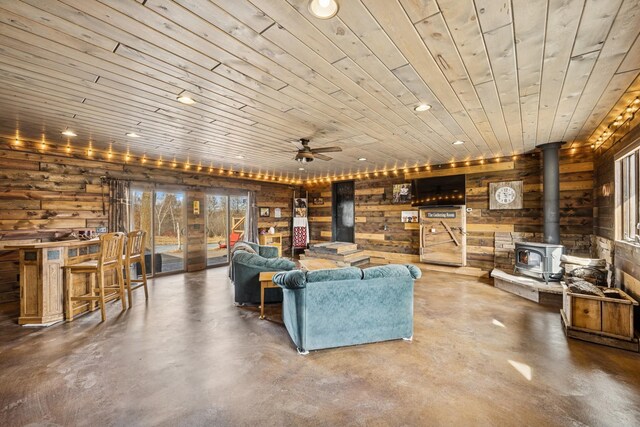 living room with ceiling fan, wooden ceiling, finished concrete flooring, and a wood stove