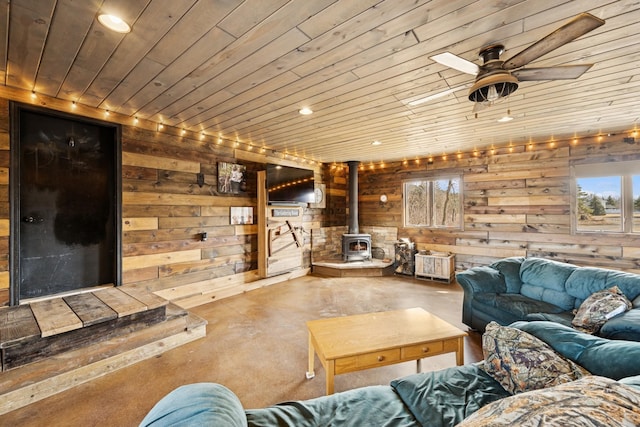 living room with wooden walls, a healthy amount of sunlight, wood ceiling, and a wood stove