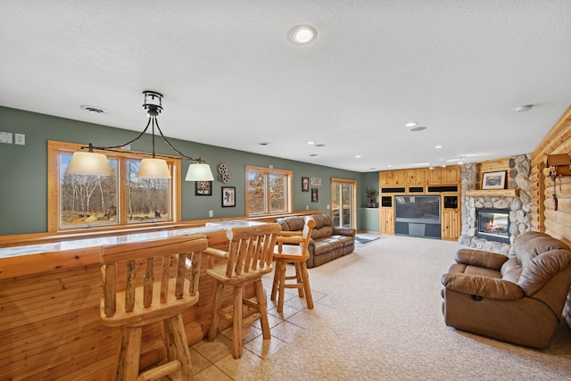 living area featuring visible vents, a textured ceiling, a bar, a stone fireplace, and light colored carpet