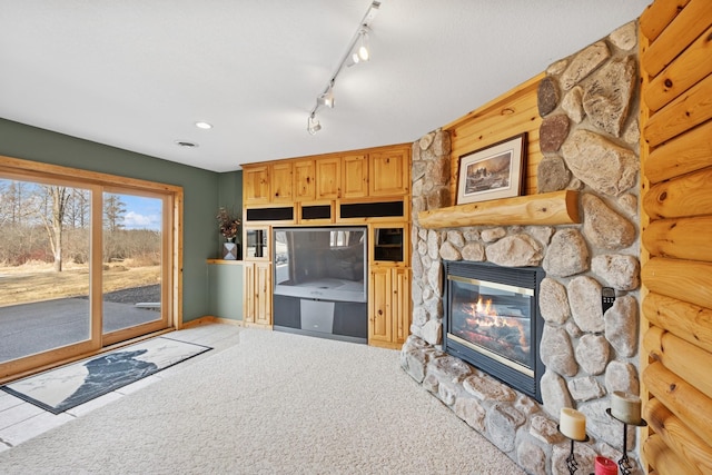 unfurnished living room featuring light carpet, a stone fireplace, track lighting, and baseboards