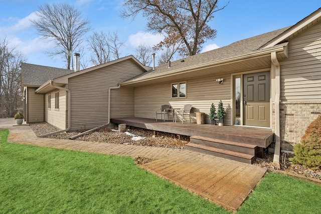 rear view of property with brick siding, a lawn, a wooden deck, and roof with shingles