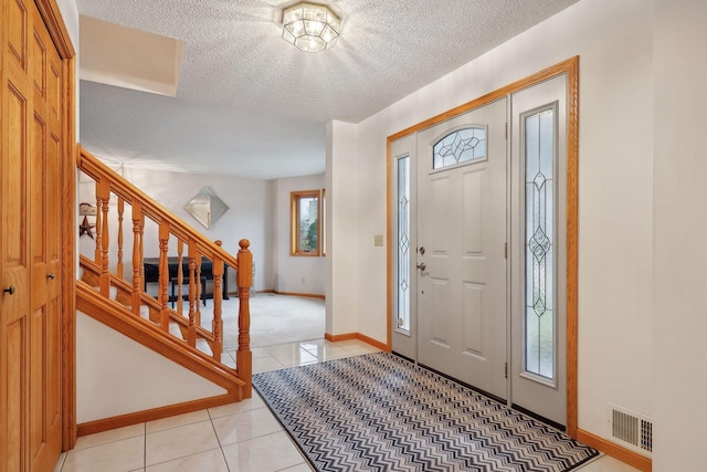 entrance foyer featuring light tile patterned floors, baseboards, visible vents, stairs, and a textured ceiling