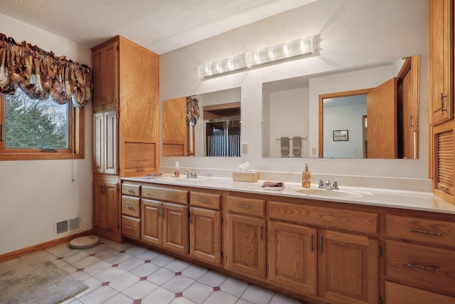 bathroom with double vanity, a textured ceiling, visible vents, and a sink