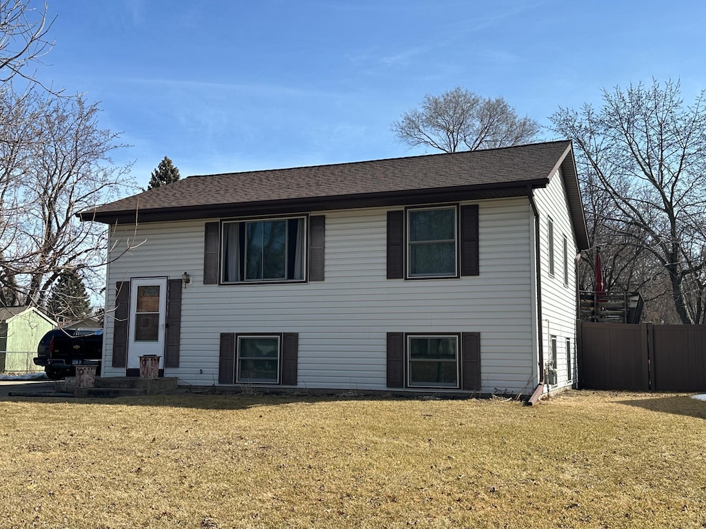 view of front of property featuring a shingled roof, a front lawn, and fence