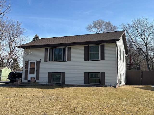 view of front of property featuring a shingled roof, a front lawn, and fence