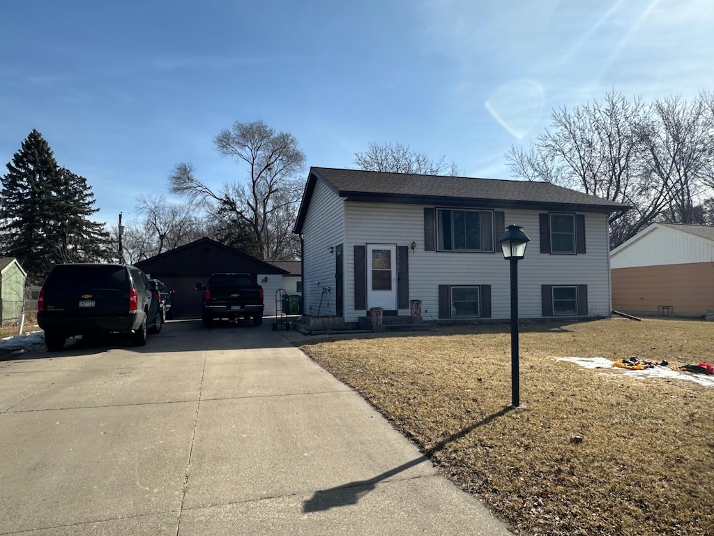 split foyer home with concrete driveway, a front lawn, and an outdoor structure