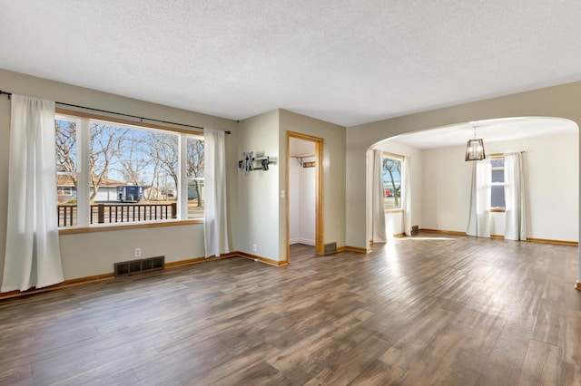 empty room with arched walkways, a textured ceiling, wood finished floors, and visible vents