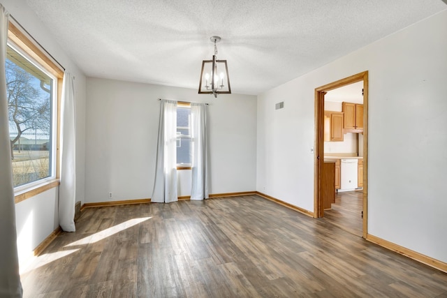 unfurnished room featuring a chandelier, wood finished floors, visible vents, and a healthy amount of sunlight