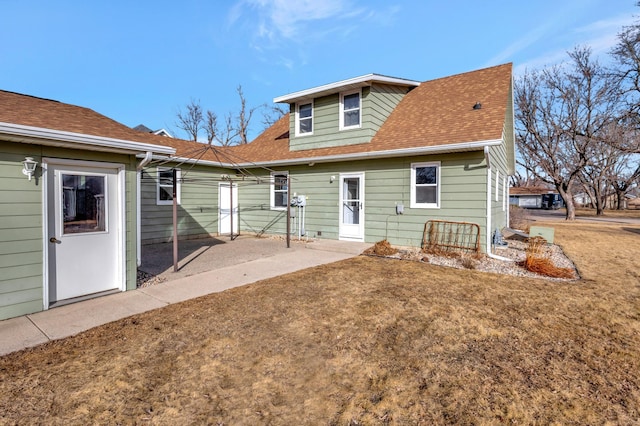 back of property with a shingled roof, a lawn, and a patio