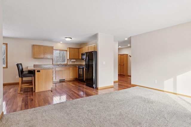 kitchen featuring a kitchen bar, black appliances, light brown cabinetry, wood finished floors, and baseboards