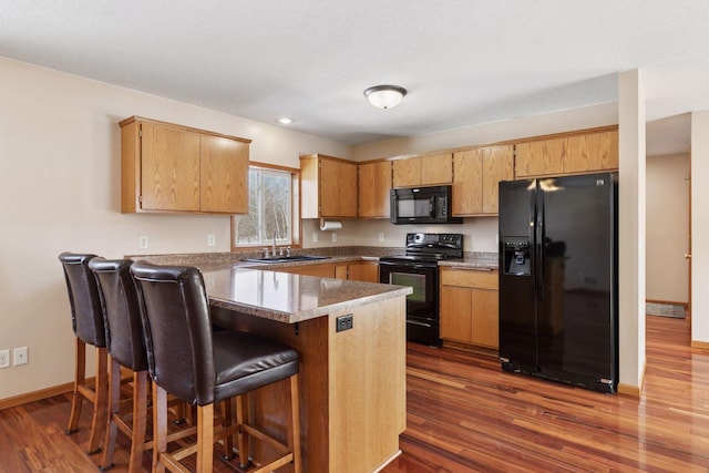 kitchen with dark wood finished floors, black appliances, a peninsula, and a sink