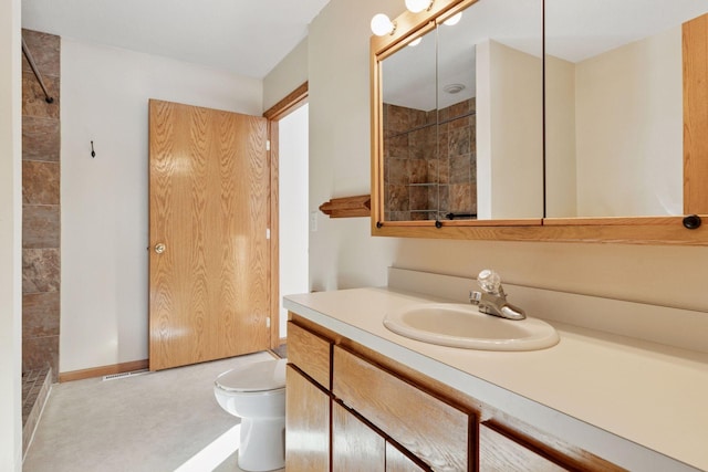 full bath featuring a tile shower, toilet, vanity, and baseboards