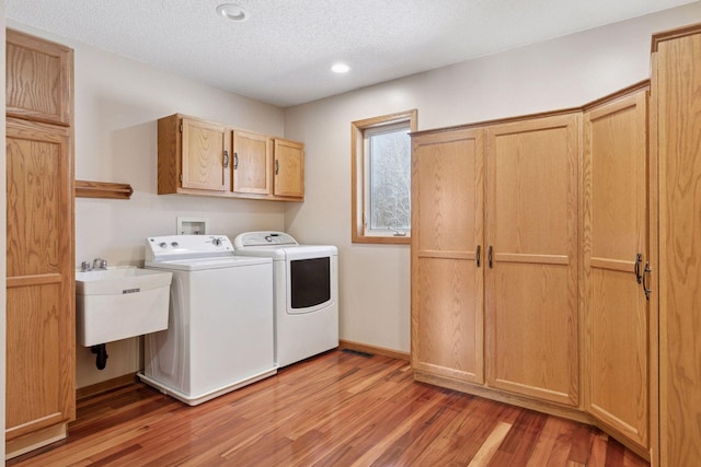 clothes washing area featuring a textured ceiling, cabinet space, separate washer and dryer, and light wood finished floors