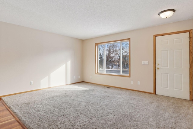 spare room featuring visible vents, light colored carpet, baseboards, and a textured ceiling