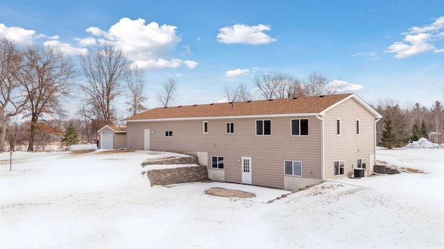 snow covered house featuring a garage, central air condition unit, and an outdoor structure