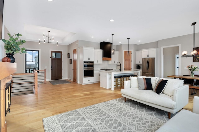 living room with a tray ceiling, a notable chandelier, recessed lighting, light wood-style floors, and baseboards