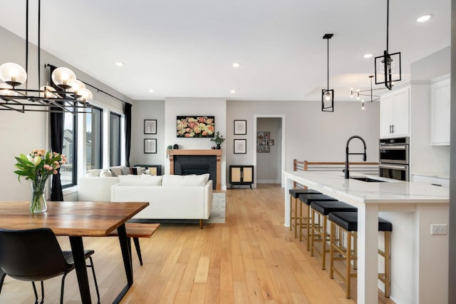 kitchen featuring light wood finished floors, a fireplace, white cabinetry, a sink, and recessed lighting