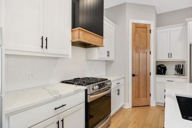 kitchen with light stone counters, white cabinets, custom exhaust hood, stainless steel gas stove, and light wood finished floors