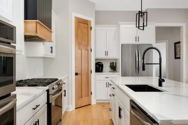 kitchen featuring light wood finished floors, decorative backsplash, white cabinets, appliances with stainless steel finishes, and a sink